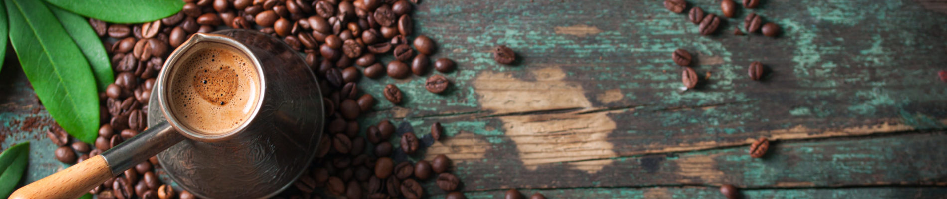 Hot coffee in a coffeepot or turk on a wooden background with coffee leaves and beans, horizontal with copy space. Top view